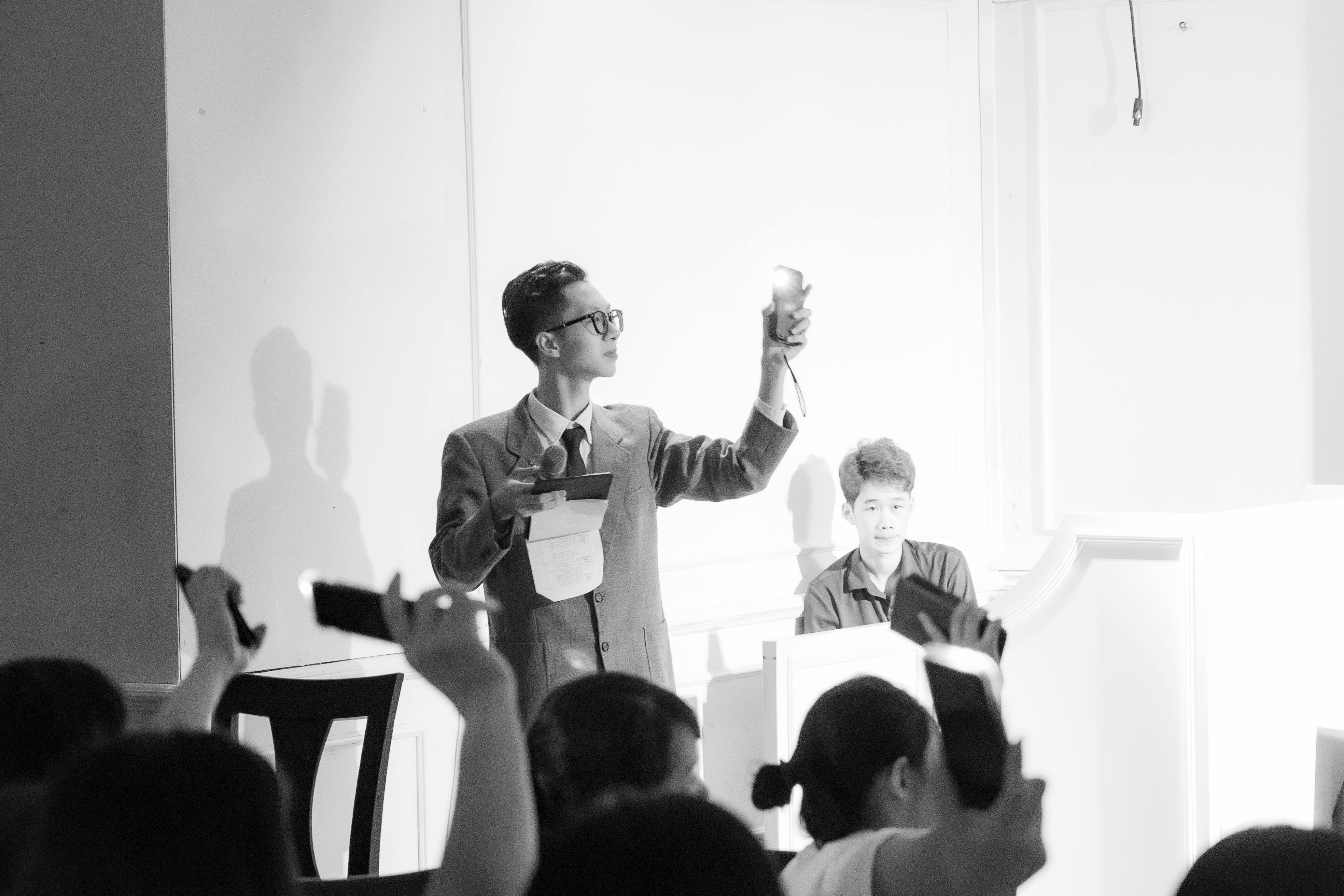 Elegant black and white photo of an auction scene with a presenter and bidders raising phones.